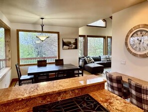 A kitchen with a granite countertop, a dining table, and chairs. There is a large window with a view of trees. - Full Cabin Near Yellowstone & Teton National Parks (Ashton)