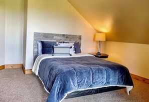 Ein Schlafzimmer mit Bett, Nachttisch, Lampe und schrägverdeckter Decke.
