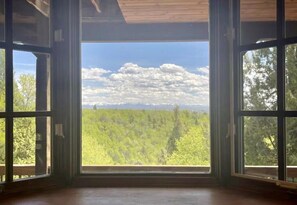 A room with large windows offering a view of a forested landscape. - Full Cabin Near Yellowstone & Teton National Parks (Ashton)
