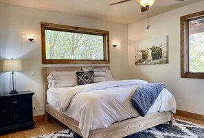 A bedroom with a bed, a nightstand, a window, and a wall-mounted artwork. - Full Cabin Near Yellowstone & Teton National Parks (Ashton)