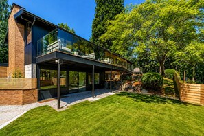 Ein modernes Haus mit Glasfassade, einer überdachten Terrasse und einem gepflegten Rasen.