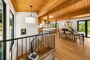 Ein modernes Interieur mit einer Treppe, einer Holzbalkendecke und einem Essbereich mit Tageslicht.