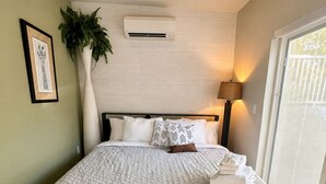 Ein Schlafzimmer mit Bett, großem Fenster, Deckenventilator und Wandklimaanlage.