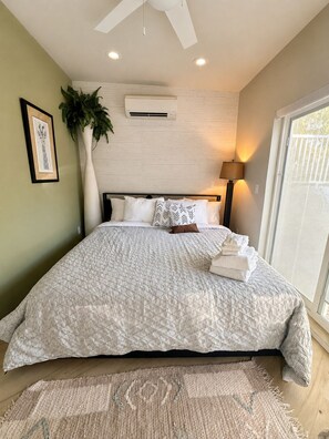 A bedroom with a bed, a large window, a ceiling fan, and a wall-mounted air conditioner. - The Haven - Downtown Egg Harbor Retreat (Egg Harbor)