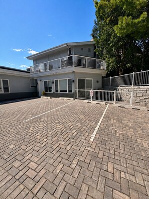 A two-story building with a brick-paved courtyard, a balcony with a railing, and a stone wall. - The Haven - Downtown Egg Harbor Retreat (Egg Harbor)