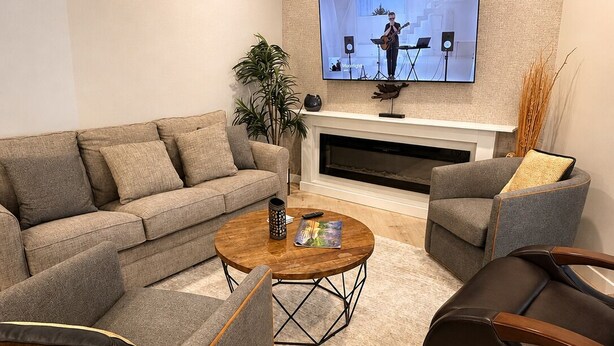 Ein modernes Wohnzimmer mit einer Couch, Sesseln, einem Couchtisch und einem flachbildfernseher an der Wand.