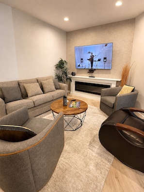 A modern living room with a sofa, armchairs, a coffee table, and a flat-screen TV mounted on the wall.