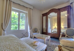 Habitació d'hotel amb un llit, una taula petita, una cadira, un mirall i una finestra amb cortines.