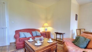 A living room with a red sofa, a wooden coffee table, and a lamp. - The Cottage - ANDERT AND CONDON (ANDERT ET CONDON)
