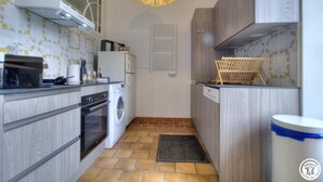 A compact kitchen with a washing machine, oven, and a hanging light fixture. - The Cottage - ANDERT AND CONDON (ANDERT ET CONDON)