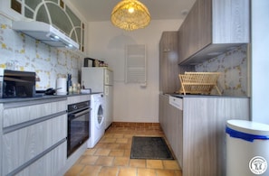 A compact kitchen with a washing machine, oven, and a hanging light fixture. - The Cottage - ANDERT AND CONDON (ANDERT ET CONDON)