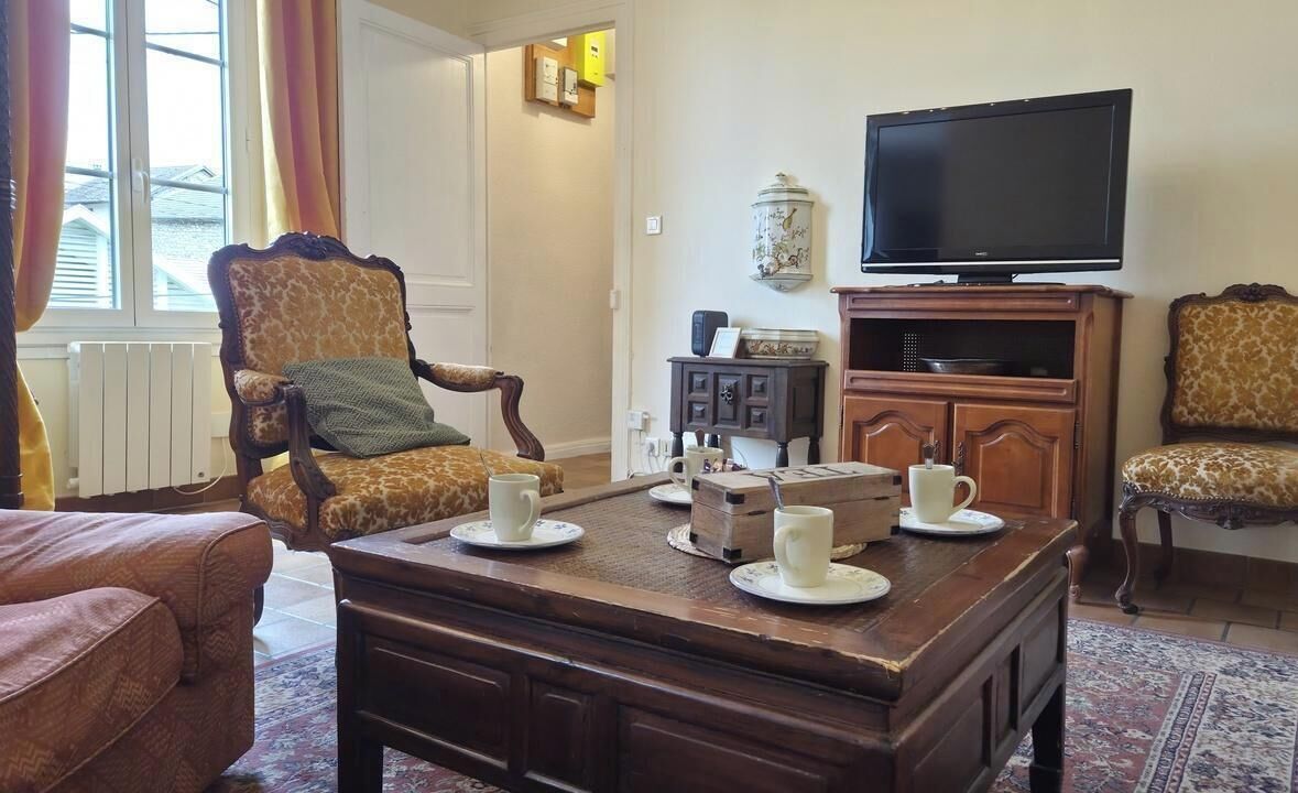 A living room with a sofa, armchairs, a coffee table with cups, a television, and a cabinet.