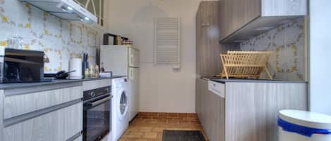 A compact kitchen with a washing machine, oven, and a hanging light fixture.