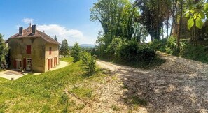 Ein rustikales Haus mit einem Feldweg, umgeben von Grün und Bäumen.