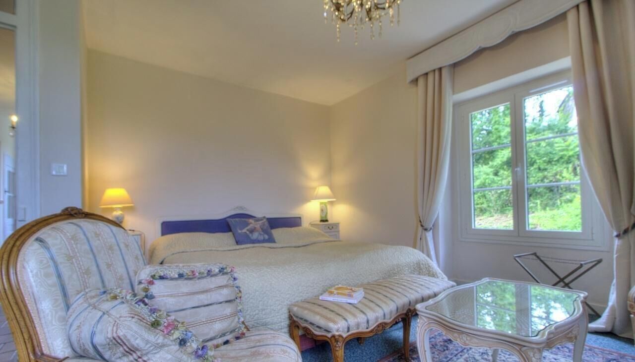 Une chambre à coucher avec un lit, des lampes de chevet, une chaise, une table et une fenêtre avec des rideaux.