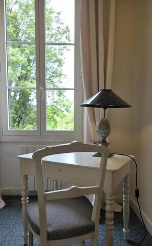 Ein Zimmer mit Fenster, Tisch, Stuhl und Lampe.