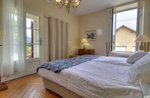 A bedroom with a bed, a window, curtains, a lamp, and a picture on the wall. - Arnaud Guesthouse – ANDERT AND CONDON (ANDERT ET CONDON)