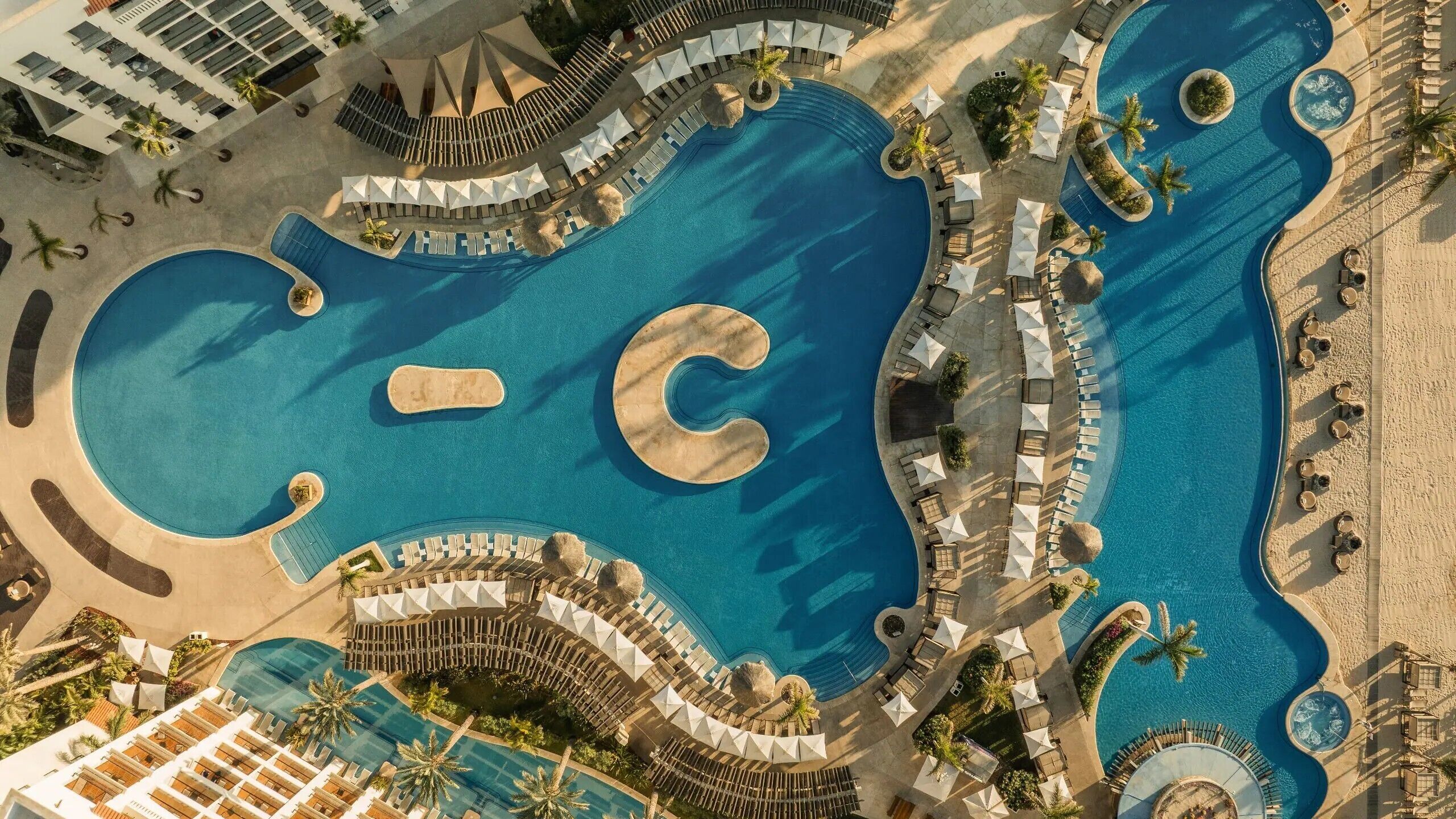 Una vista aerea di un resort con piscine, lettini e ombrelloni.