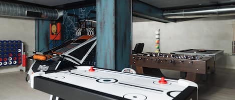 A pool table, a foosball table, and a basketball hoop in a recreational area.