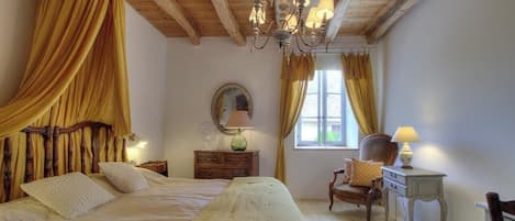 A bedroom with a bed, a wooden headboard, a chandelier, a dresser, a chair, and a window with curtains.