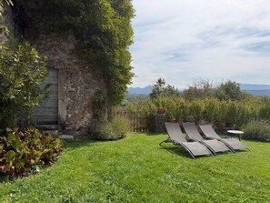 Un mur de pierre avec une porte en bois, une pelouse verdoyante et deux fauteuils de jardin.