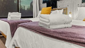A hotel room with two beds, each with a white bedspread and a purple blanket. There are stacks of white towels on each bed. - Lux SLC - Pool - Gym - Rooftop (Salt Lake City)
