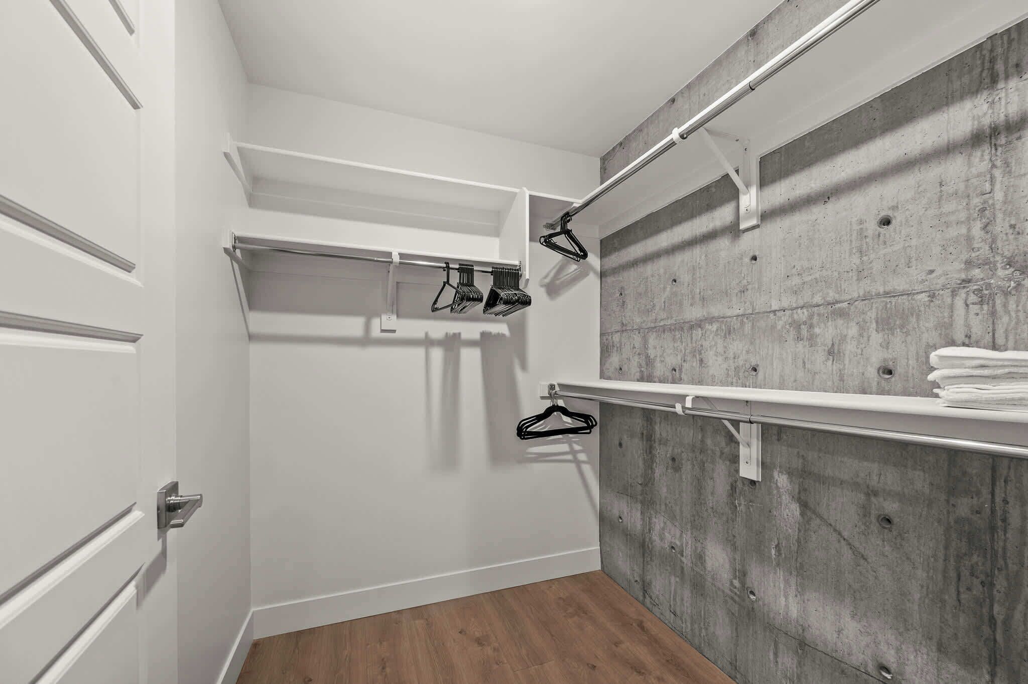 A walk-in closet with a wooden floor, white doors, and a concrete wall.