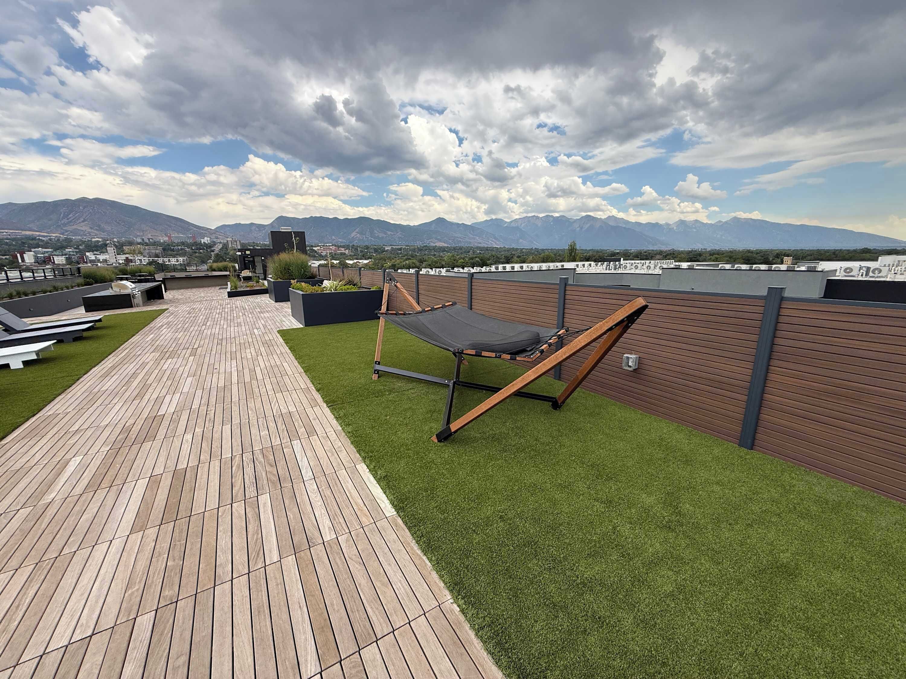 Um terraço no telhado com um deck de madeira, uma rede e vista para montanhas ao longe.