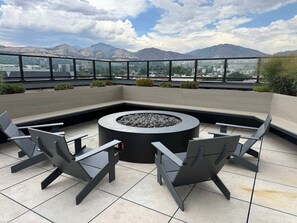 A rooftop terrace with a circular fire pit, seating, and a view of mountains. - Lux SLC - Pool - Gym - Rooftop (Salt Lake City)