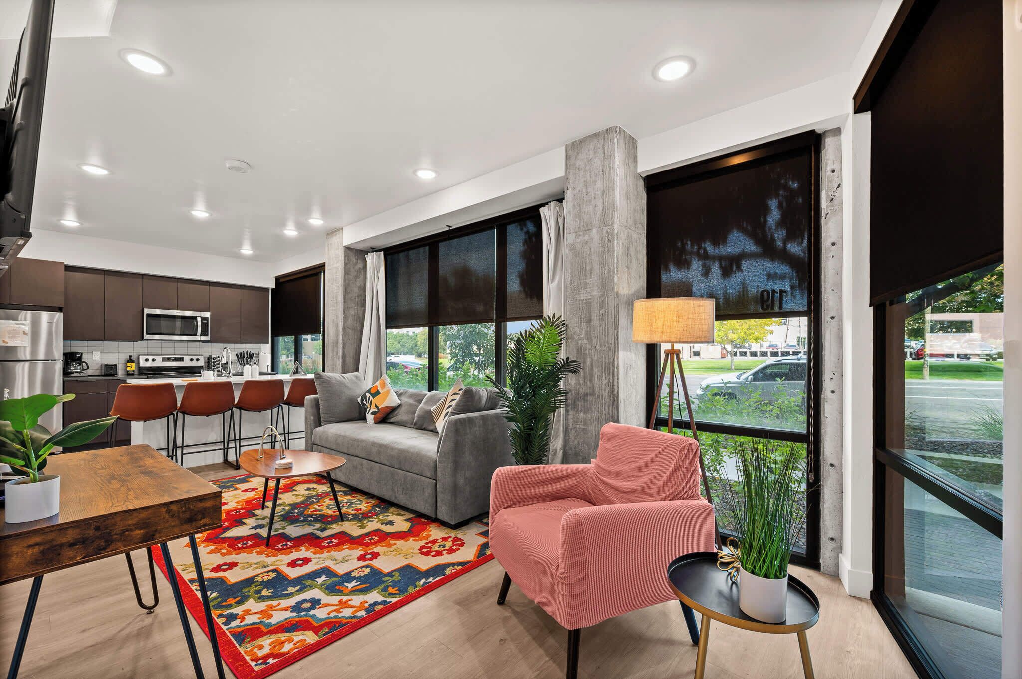 Uma sala de estar moderna com um sofá cinzento, uma poltrona vermelha e um espaço de refeições com uma mesa e cadeiras de madeira.