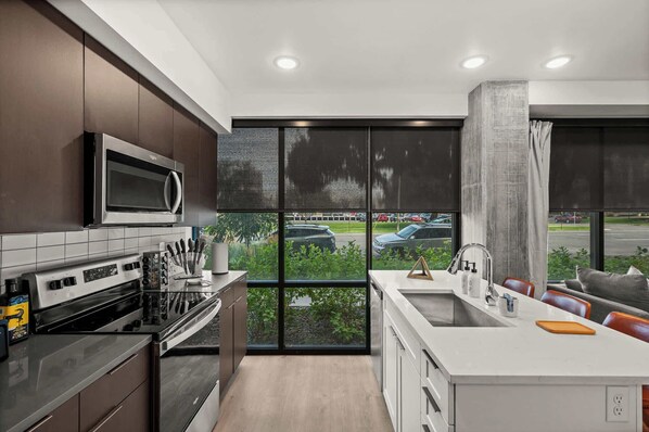A modern kitchen with a large window, stainless steel appliances, and a view of a parking lot.