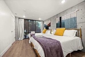 A modern bedroom with two beds, a large window, and a view of trees. - Lux SLC - Pool - Gym - Rooftop (Salt Lake City)