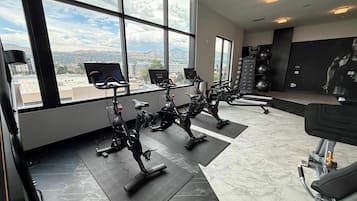 A gym with stationary bikes, exercise mats, and a large window with a city view.