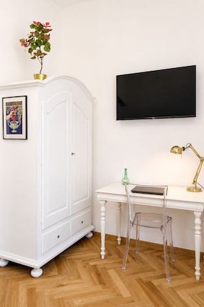 A room with a white wardrobe, a desk with a laptop, a green vase, a clear chair, a gold lamp, and a framed picture on the wall. - Caramanna Studio Apartment (Bologna)