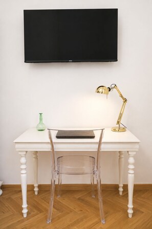 Un bureau blanc avec un ordinateur portable, une lampe de bureau dorée et un vase vert.