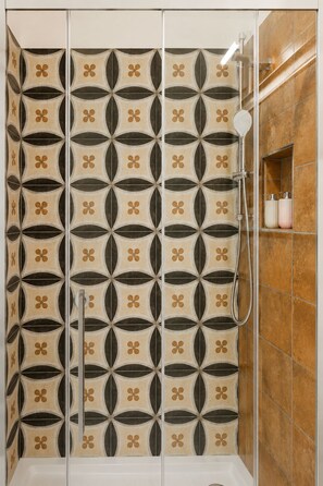Une cabine de douche avec un motif géométrique en carreaux et un pommeau de douche à main.