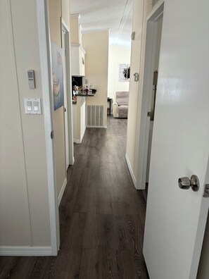 Ein Flur mit Holzboden, ein Küchenbereich mit Esstisch und Stühlen sowie ein Wohnzimmer mit einer Couch.
