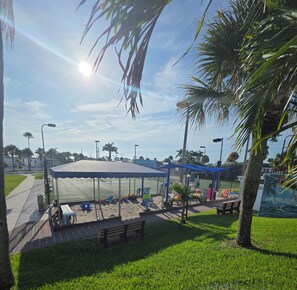 Ein sonniger Außenbereich mit überdachter Sitzgelegenheit, einem eingezäunten Sportplatz und Palmen.