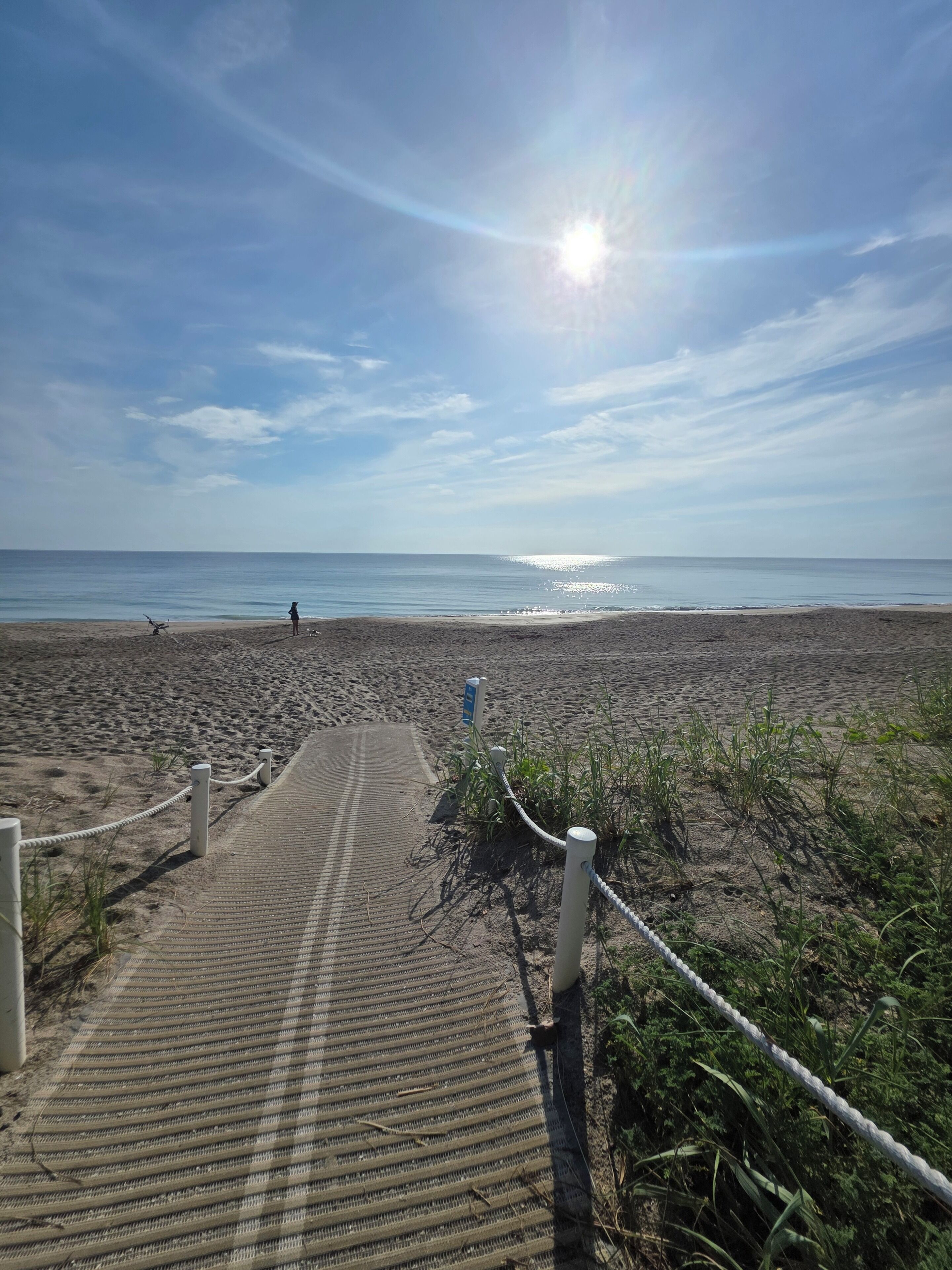 Une plage avec une promenade en bois menant à l’eau, une barrière faite de cordes et un ciel dégagé.