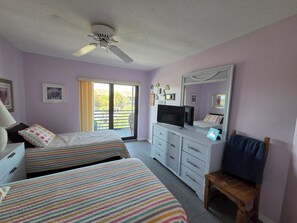 A bedroom with two beds, a ceiling fan, a television, and a sliding glass door leading to an outdoor area. - Manasota Key FI Getaway (Englewood)