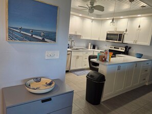 A modern kitchen with white cabinets, a microwave, and a sink. There's a painting of seagulls on the wall and a bowl on a counter. - Manasota Key FI Getaway (Englewood)