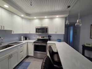 Cozinha moderna com armários brancos, eletrodomésticos de aço inoxidável e um tapete azul.