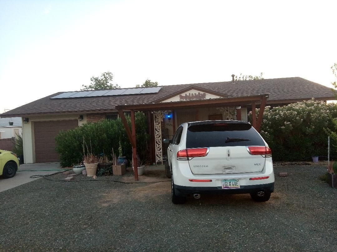 En hvid SUV parkeret foran et hus med garage, solpaneler på taget og en overdækket veranda.