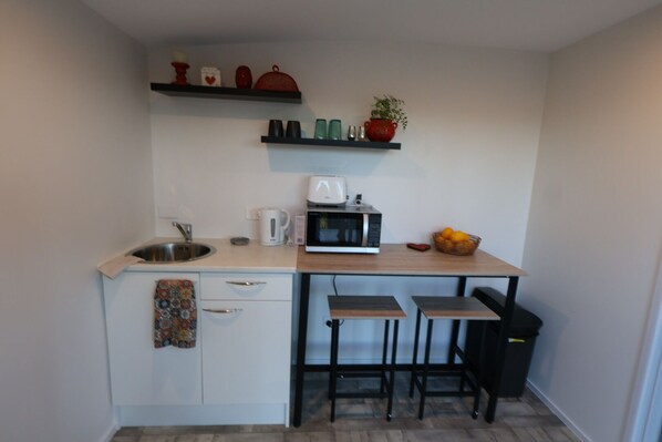 A compact kitchen with a microwave, kettle, and a small fruit basket.