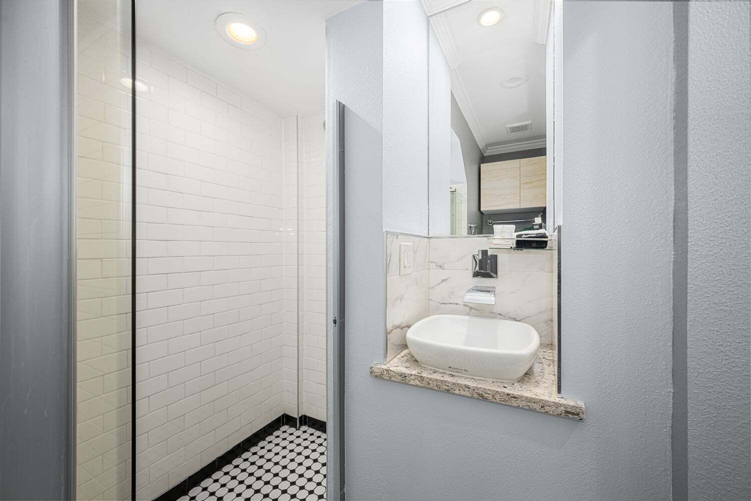 A modern bathroom with a white tiled shower, a white sink with a marble countertop, and a mirror.