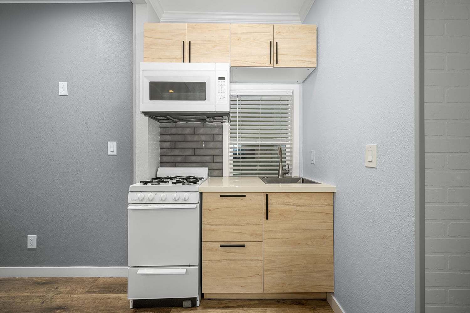Una cucina compatta con fornello a gas, forno a microonde bianco e mobili in legno.