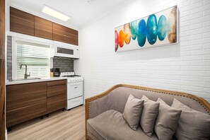 A modern kitchen with white appliances, wooden cabinets, and a beige sofa in a living area. - West Oceanfront Oasis 1-8-9 (Newport Beach)