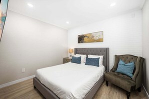 A bedroom with a bed, a nightstand, a chair, and a painting on the wall. - West Oceanfront Oasis 1-8-9 (Newport Beach)