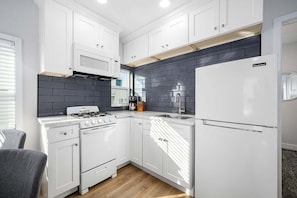 Une cuisine moderne avec des meubles blancs, une cuisinière à gaz, un four encastré, un réfrigérateur et un dosseret de carrelage noir.