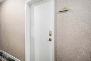 Een witte deur met een keypad slot en een sleutelgat, in een gang met beige, gestructureerde wanden.